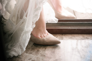 Fototapeta premium The legs of the bride in a wedding dress in shoes