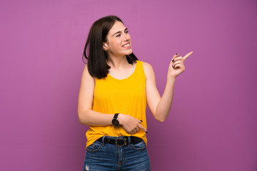 Fototapeta premium Young woman over isolated purple wall pointing finger to the side