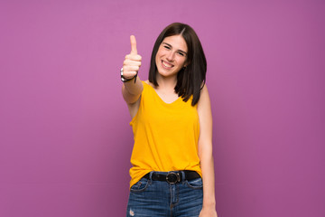 Young woman over isolated purple wall with thumbs up because something good has happened