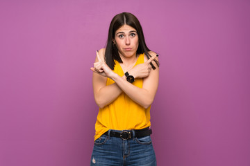 Young woman over isolated purple wall pointing to the laterals having doubts