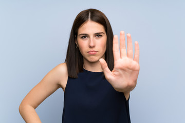 Young woman over isolated blue wall making stop gesture with her hand