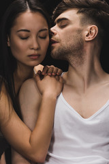 handsome man kissing beautiful asian woman lying on his shoulder isolated on black