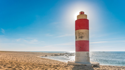 Fototapeta premium Lighthouse on beach in summer with sun producing halo effect