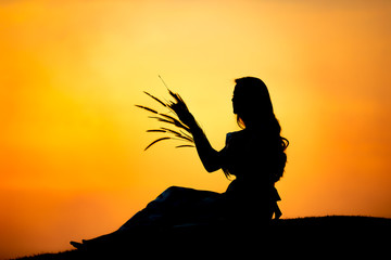 silhouette women sitting with grass on holding hand relax time and the sunset background