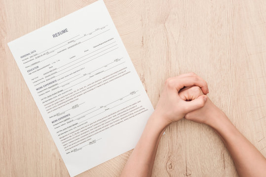 partial view of recruiter holding clenched hands near resume template on wooden table