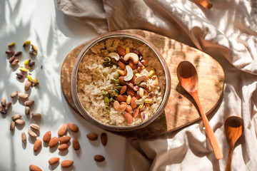 Oatmeal porridge in coconut bowl with wooden spoon on natural wooden tray. Porridge oats with...