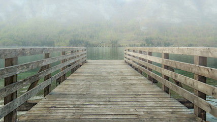 Fototapeta premium Pier on lake Bohinj. Fog over the water hides mountain at another bank of the lake.