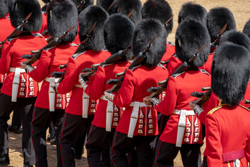 Close up of soldiers marching at the Trooping the Colour military parade at Horse Guards, London UK. Guards are wearing iconic black and red uniform and bearskin hats.