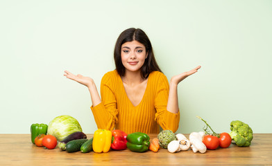 Fototapeta premium Teenager girl with many vegetables having doubts while raising hands