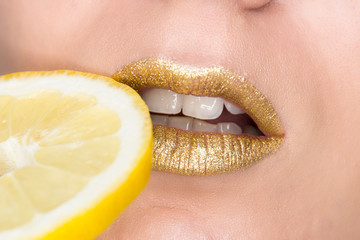 Beautiful closeup with female lips with gold color makeup and lemon slice. Glitter cosmetics