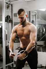 Muscular young man working in gym doing exercises at triceps