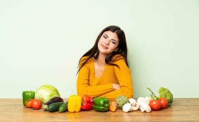 Fototapeta premium Teenager girl with many vegetables with arms crossed and looking forward