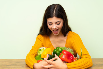 Fototapeta premium Surprised teenager girl with many vegetables over green wall