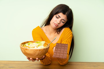 Teenager girl with salad and chocolat having doubts