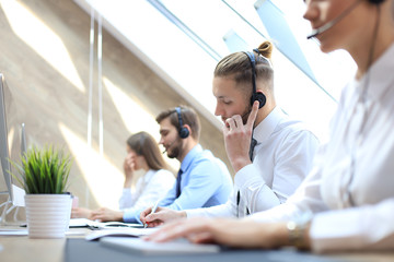 Obraz premium Portrait of call center worker accompanied by his team. Smiling customer support operator at work.