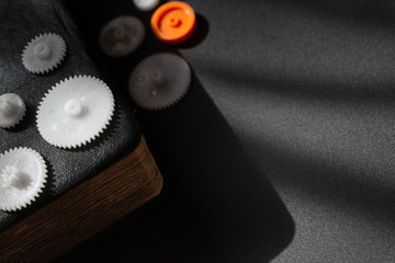 Corner of thick diary with leather cover and gilded sheets. Colored cogwheels is on the notebook. Place for caption.