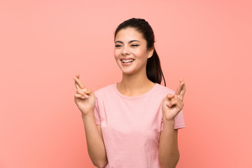 Teenager girl over isolated pink background with fingers crossing