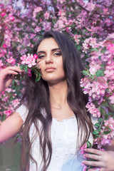 Fototapeta premium Sensual portrait of a spring woman, beautiful face, close up on blue eyes, female enjoying cherry blossom, dreamy girl with pink fresh flowers outdoor, seasonal nature, tree branch and natural beauty