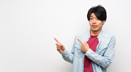 Asian man on isolated white background frightened and pointing to the side