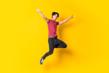 Asian man jumping over isolated yellow wall