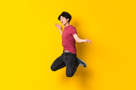 Asian Man Jumping Over Isolated Yellow Wall