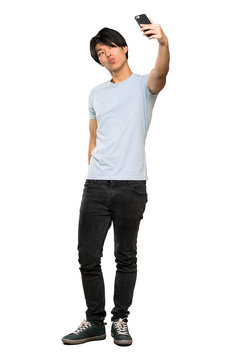 A full-length shot of a Asian man with blue shirt making a selfie over isolated white background