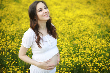 Naklejka na ściany i meble Pregnant woman in a dress in a field of flowers
