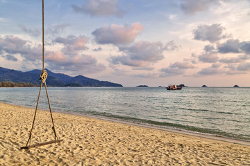 wooden swing hang from a tree on a beach and sunset