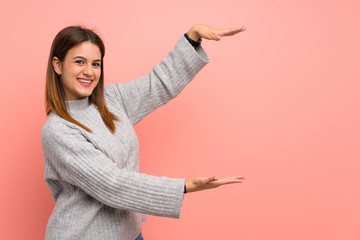 Young woman over pink wall holding copyspace to insert an ad