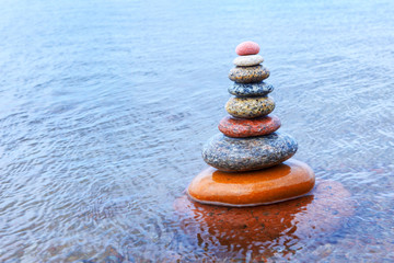 Fototapeta na wymiar Rock Zen pyramid of colorful pebbles standing in the water