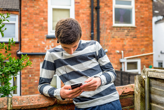 teen boy with smart phone listening or talking while sitting in british backyard garden. teenager and social media concept