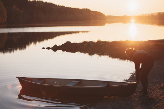 young man puts a canoe boat in the water at sunset with a beautiful landscape in the background.