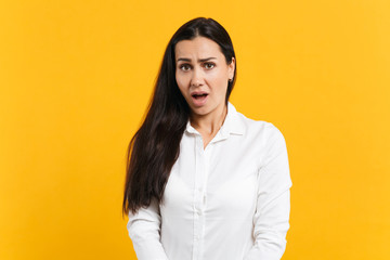 Portrait of irritated disconcerted young woman in white casual shirt looking camera, swearing isolated on bright yellow orange wall background in studio. People lifestyle concept. Mock up copy space.