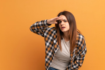 Young woman over brown wall looking far away with hand to look something