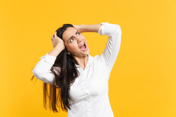 Portrait of irritated angry young woman in white casual shirt looking aside, putting hands on head isolated on yellow orange wall background in studio. People lifestyle concept. Mock up copy space.