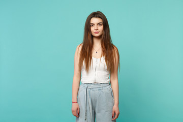 Portrait of beautiful young woman in light casual clothes standing, looking camera isolated on blue turquoise wall background in studio. People sincere emotions, lifestyle concept. Mock up copy space.