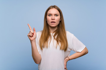 Fototapeta premium Young woman over blue wall thinking an idea pointing the finger up