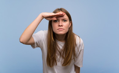 Young woman over blue wall looking far away with hand to look something
