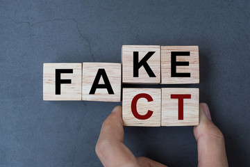 Business man hand holding wooden cube with flip block FAKE to FACT word on table background. News,...