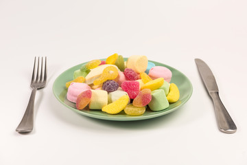 Fork, knife and plate with marshmallow and gummy candies isolated on white background.