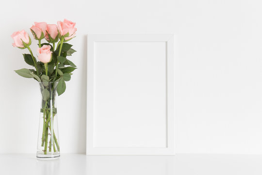 White frame mockup with a bouquet of pink roses in a glass vase on a white table. Portrait orientation.