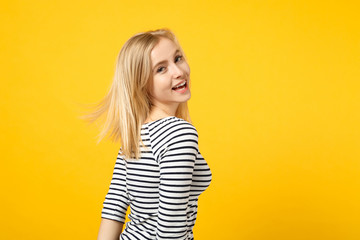 Portrait of cheerful beautiful laughing young woman in striped clothes looking back isolated on yellow orange wall background in studio. People sincere emotions, lifestyle concept. Mock up copy space.