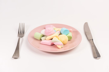 Fork, knife and pink plate with marshmallow isolated on white background.