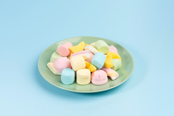 Green plate with marshmallow isolated on blue background.