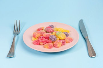 Fork, knife and pink plate with gummy candies isolated on blue background