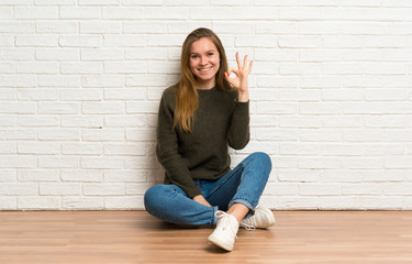 Young woman sitting on the floor showing ok sign with fingers
