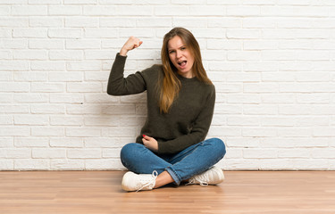 Young woman sitting on the floor doing strong gesture