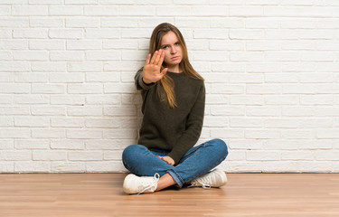 Fototapeta na wymiar Young woman sitting on the floor making stop gesture