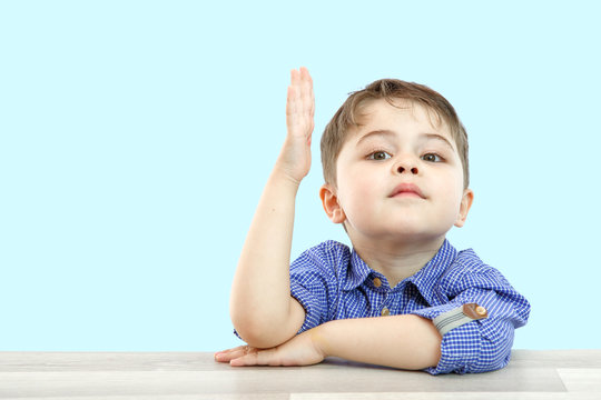 little boy of preschool age raises his hand to answer the question or ask the question. on an isolated background