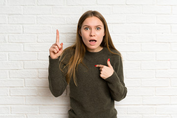 Young woman over white brick wall with surprise facial expression